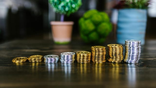 Close-up of stacked gold and silver bitcoins on a wooden table with plants in the background.