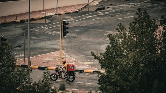 Pizza delivery on a scooter in the streets of Kuwait City. Aerial view shows urban life and transportation.