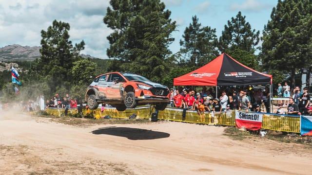 A thrilling rally car in midair during a crowded motorsport event in Sardinia, Italy.