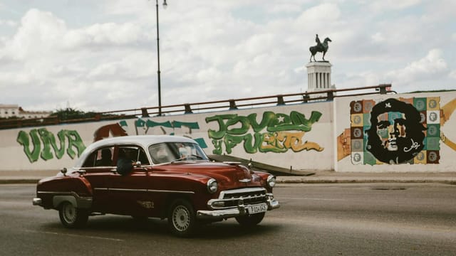 Classic Chevrolet car cruising past Havana street art with Che Guevara mural.