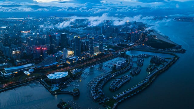 Dusk aerial view of Xiamen, China, showcasing modern skyline, marina, and coastline.