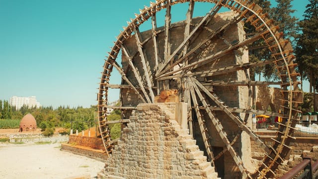 View of the ancient Norias in Hama, Syria, showcasing their intricate wooden design against a bright sky.