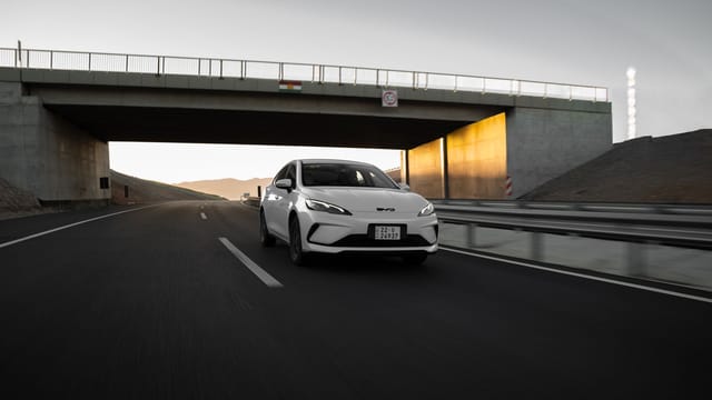 A white modern car driving under a bridge on a highway at sunset, showcasing speed and elegance.