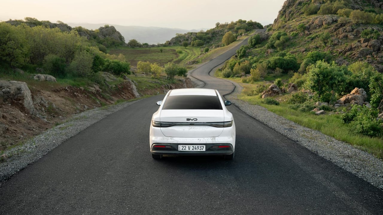 A white car travels down a winding road in the lush hills of Shaqlawa, Iraq, showcasing serene scenery.