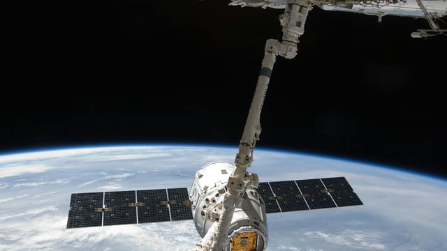 View of a spacecraft docked at the ISS above Earth with visible solar panels.