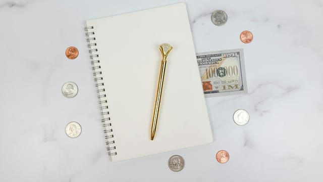 Stylish flat lay of a notebook with coins and a $100 bill on a marble surface.
