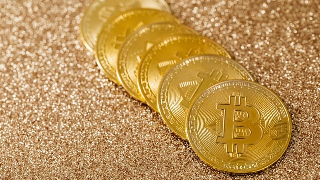 A stack of gold Bitcoin coins placed on a shimmering gold glitter background.