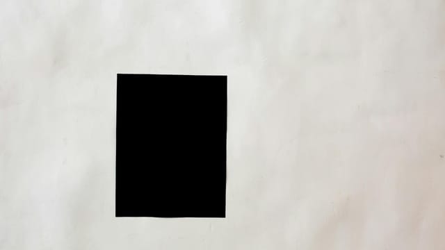 A striking minimalist black square on a textured white wall offers creative copyspace.