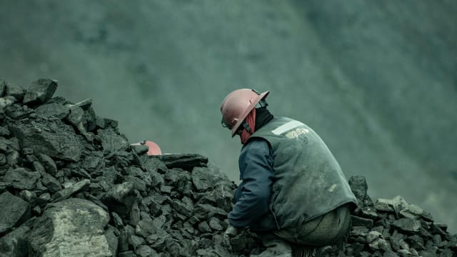 A miner wearing a helmet works in a quarry among rocks in Puno, Peru.