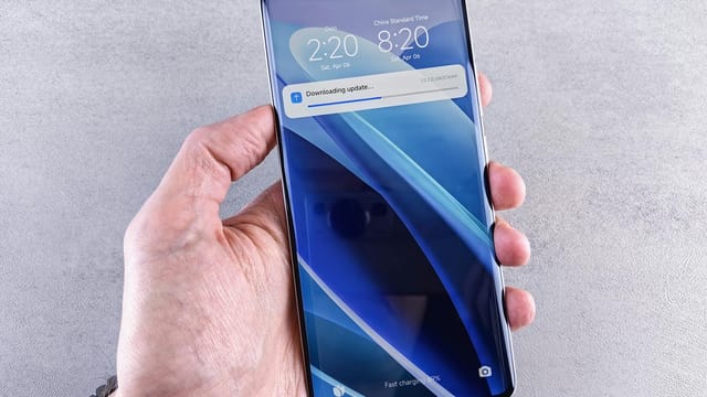 Close-up of a hand holding a smartphone with a downloading update notification on the screen.