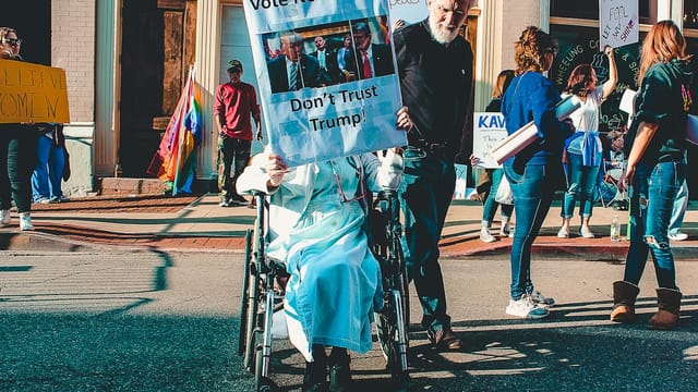 A diverse group of people protesting outdoors with signs and banners in a vibrant street scene.