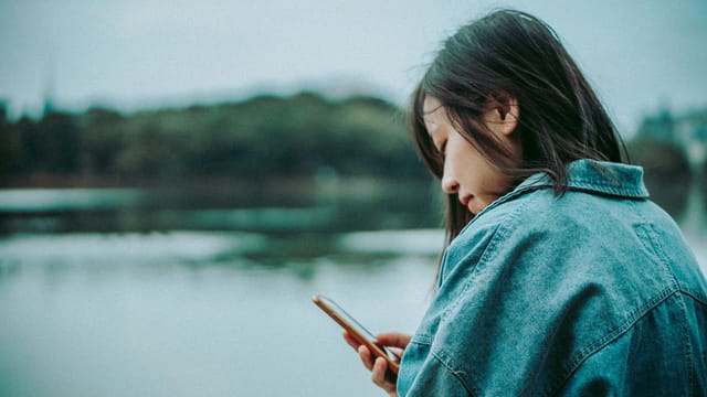 A woman enjoys a serene moment by the lake, engrossed in her smartphone.