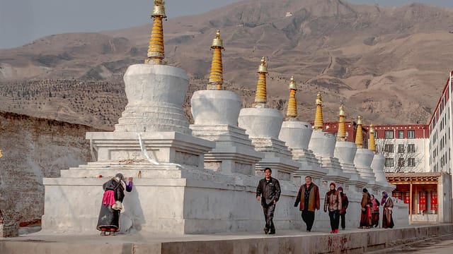 Buddhist stupas with people walking in a Tibetan landscape, capturing cultural and architectural essence.