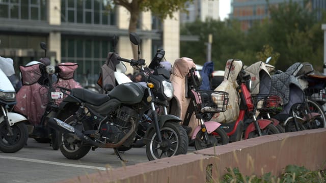 A row of parked scooters and motorcycles in an urban outdoor setting with protective covers.