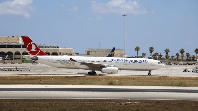 Turkish Airlines airplane taxiing on a sunny airport runway with clear skies.