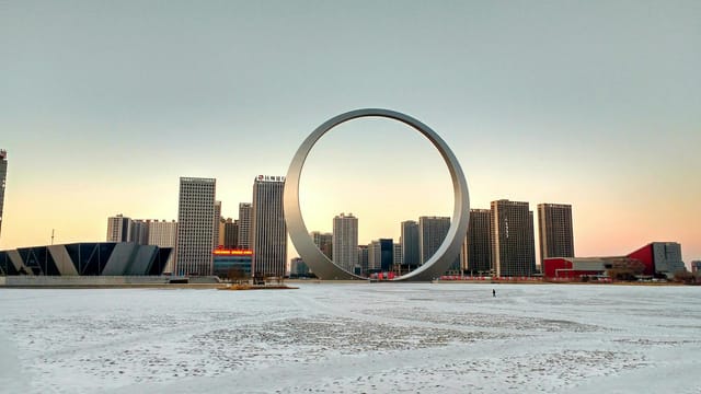 Explore the iconic Ring of Life surrounded by towering buildings in a snowy Chinese cityscape.