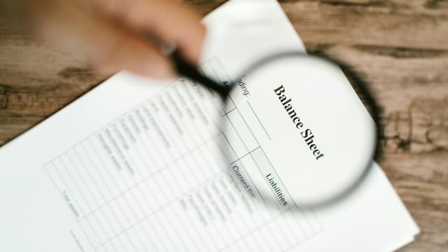 Close-up of a balance sheet under a magnifying glass on a wooden table.