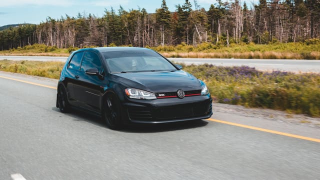 Black hatchback car speeding on a forest highway, showcasing modern design and motion.
