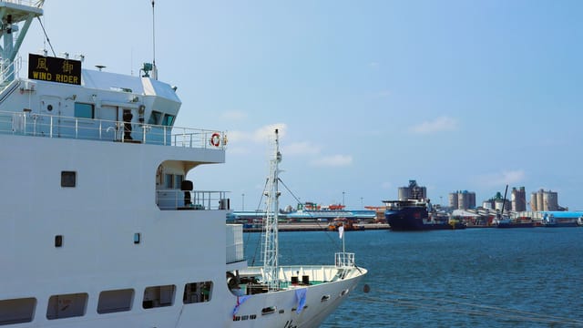 A cargo ship named 'Wind Rider' docked at a bustling port in Taiwan, showcasing industrial maritime activity.