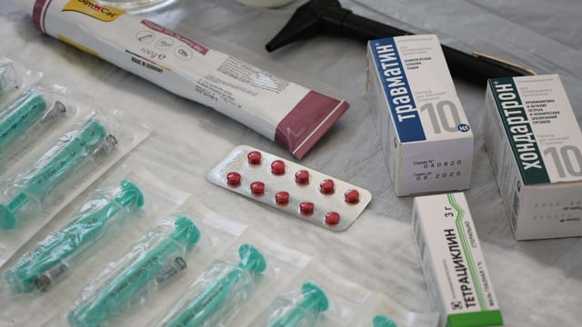 Flat lay of medical supplies including syringes, pharmaceuticals, and an otoscope on a table.