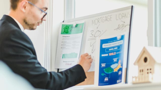 Real estate agent analyzing mortgage loan details on a whiteboard in an office setting.