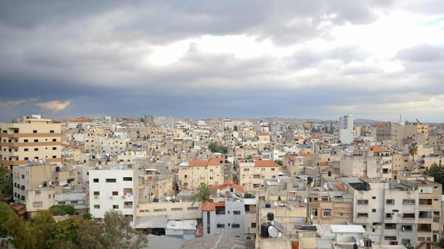 Aerial view of Qalqilya's urban cityscape under dramatic clouds, showcasing diverse architecture.