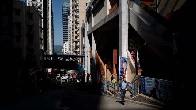 Man walking in a vibrant downtown area with tall buildings and sunlight casting shadows.