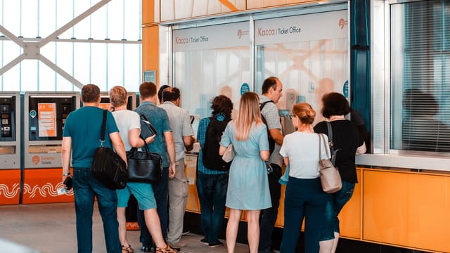 Back view of unrecognizable people in casual wear standing near ticket office in public place