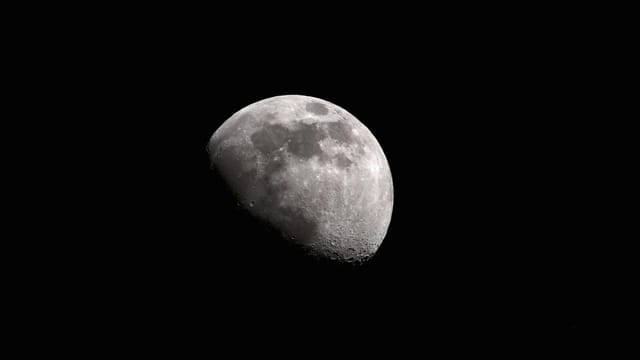 Black and white of moon with craters glowing on black sky at night