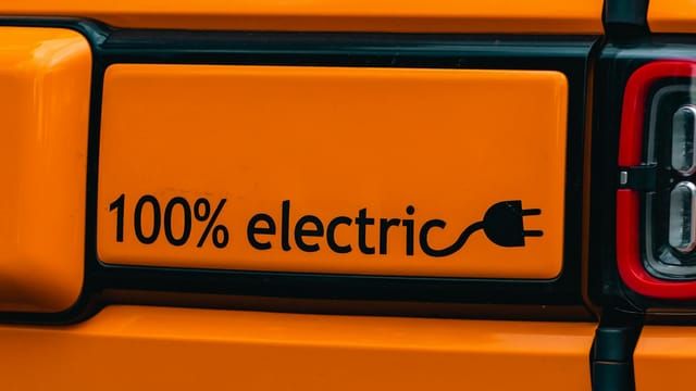 Vibrant orange electric vehicle with a '100% electric' emblem, showcasing eco-friendly transportation.