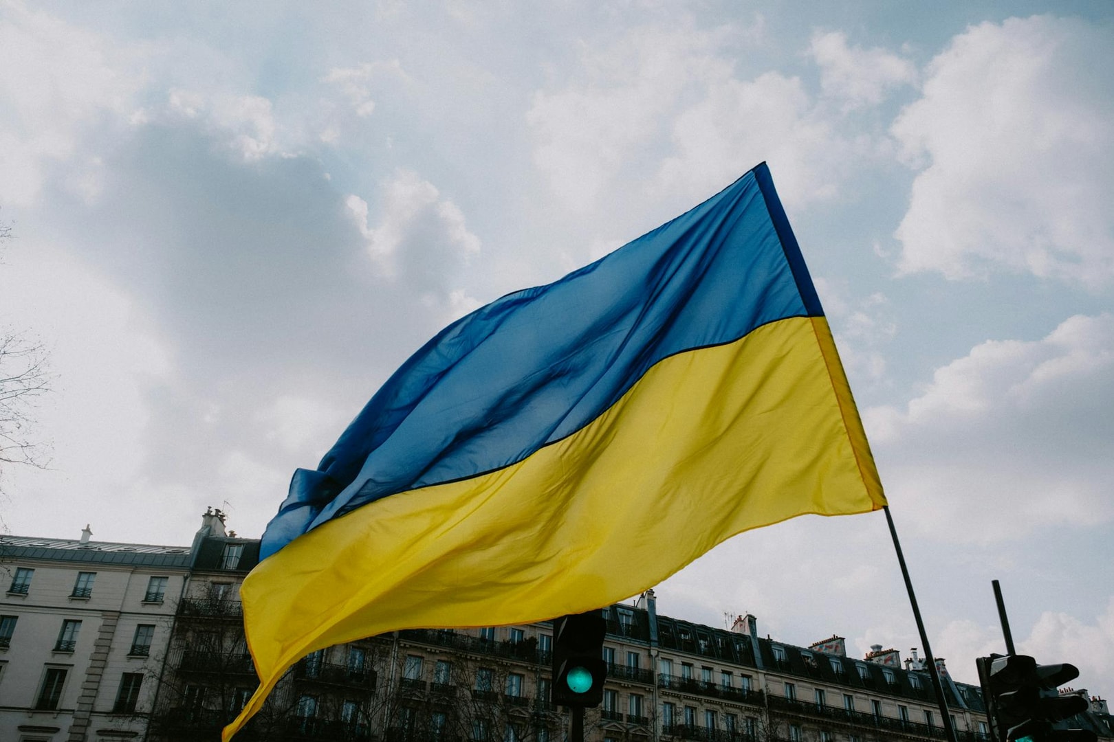 Waving Ukrainian flag against a cloudy sky and city skyline, symbolizing national pride.