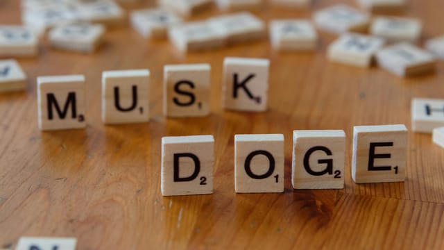 Scrabble tiles spelling 'DOGE' and 'MUSK' on a wooden table, highlighting internet culture and cryptocurrency.