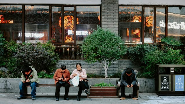 People sitting on a bench in Nanjing, China, using mobile phones, showcasing urban life.