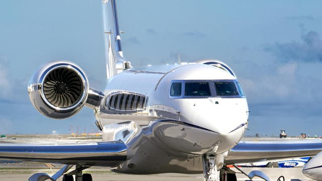 A sleek private jet parked on the tarmac with supporting ground vehicle under a clear blue sky.