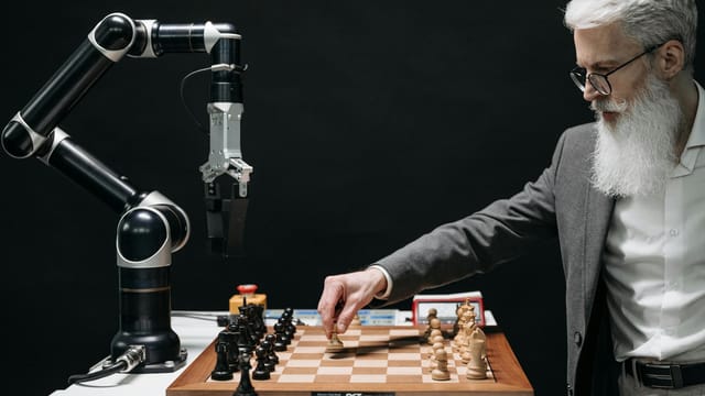 A bearded man strategically moves chess pieces while an AI robot arm assists in a futuristic game.