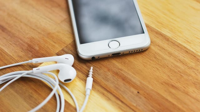 Close-up of smartphone with earphones on wooden desk, showcasing modern technology and connectivity.
