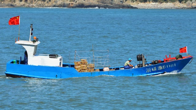 A vivid blue fishing boat with a person onboard navigates the waters near Zhoushan, China.