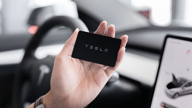 Close-up of a hand holding a key card inside a modern car interior with digital display.