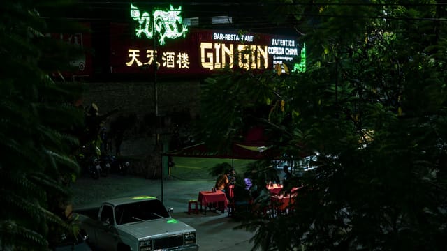 Vibrant nightlife scene in Mérida, showcasing a neon-lit street with parked cars and people enjoying dinner.