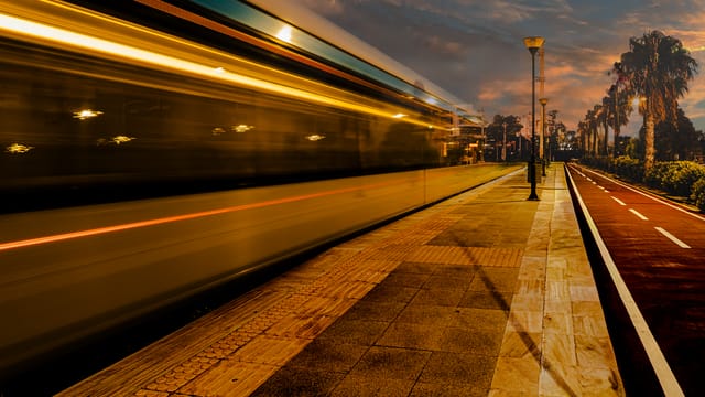 Dynamic image of a high-speed train zooming past a deserted station at sunset.