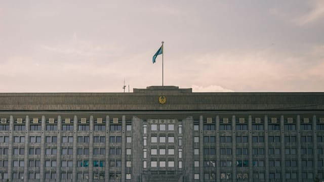 A grand government building with Kazakhstan flag in a clear sky.