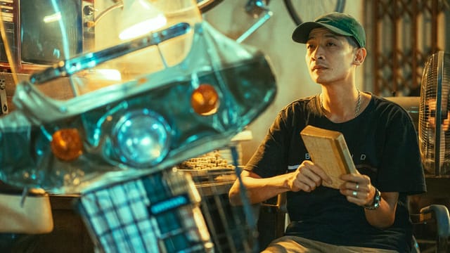 Man seated in a vintage setting with ambient lighting, holding an object.