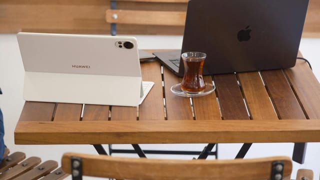 A cozy café workspace featuring a laptop with Turkish tea on a wooden table in İzmir, Türkiye.