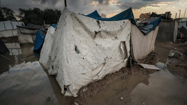 A damaged tent shelter in a flooded area of a Gaza refugee camp under stormy skies.
