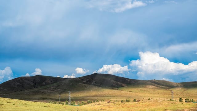 Beautiful landscape of rolling hills under a cloudy blue sky in Ulanqab, China.