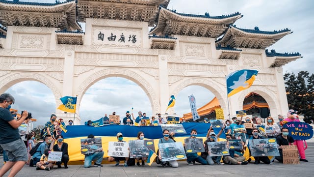 Protesters gather with Ukrainian flags at Liberty Square, advocating for peace and democracy.