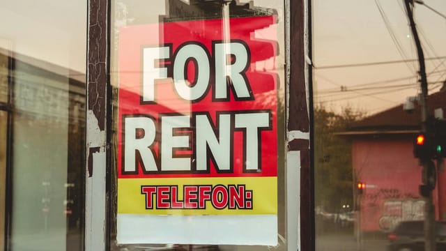 Reflection of a cityscape on a window with a 'For Rent' sign and sunset glow.