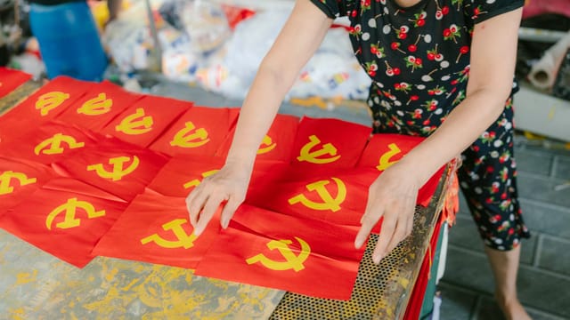 A person arranges red flags featuring the yellow hammer and sickle emblem indoors.