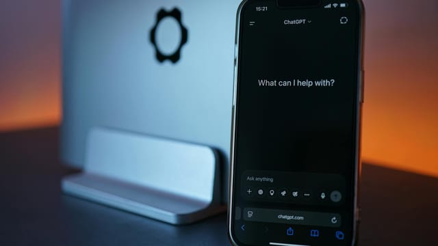Close-up of a smartphone showing a chat interface with a laptop in the background.