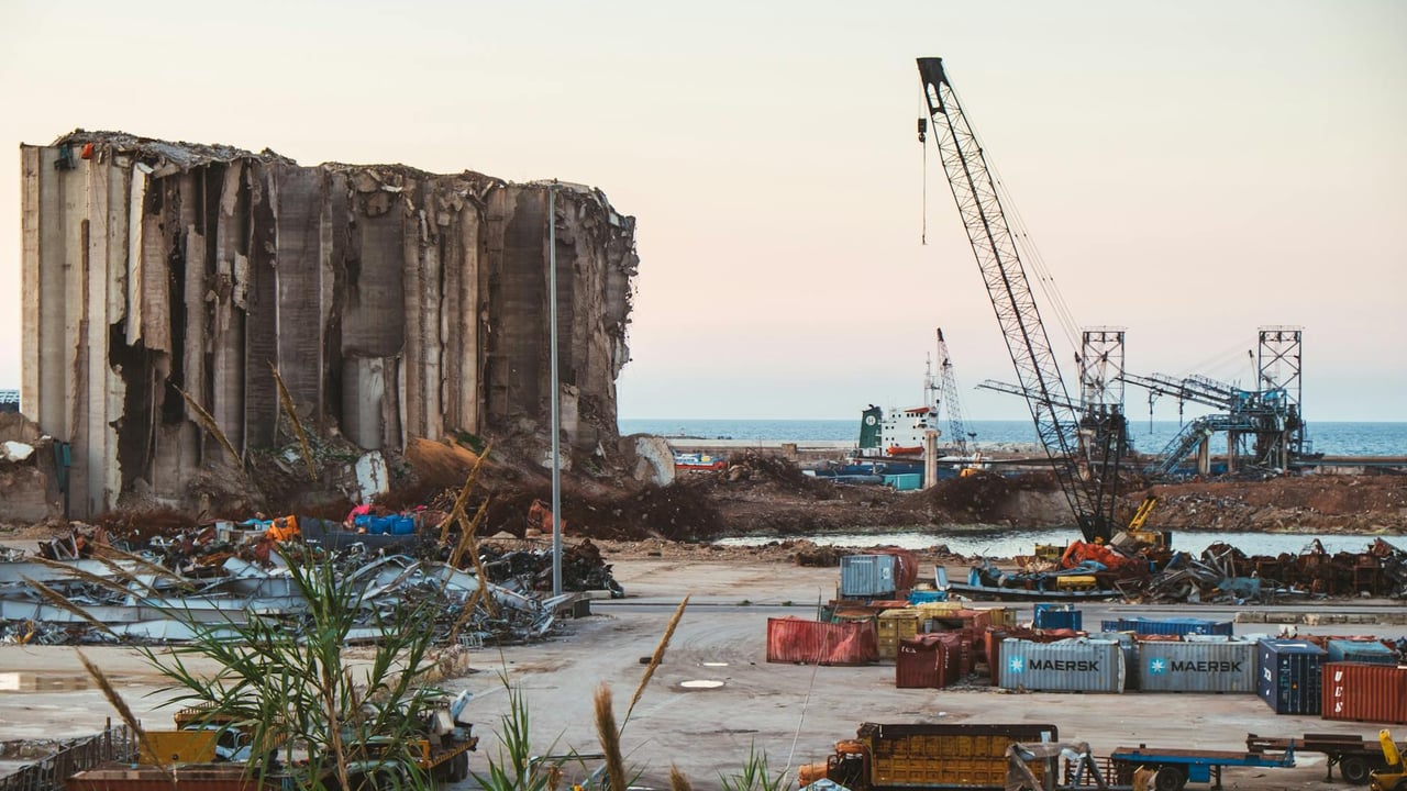View of destruction and debris at Beirut port with cranes and sea in the background.